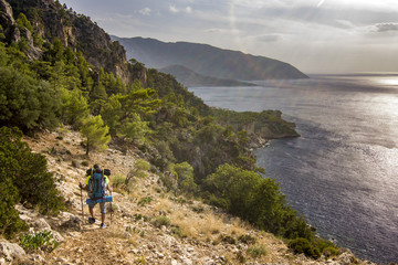 Fototapeta premium tourist with backpack standing on a cliff in mountains near mediterranean sea