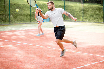 Young couple in white sports wear playing tennis on the tennis court outdoors