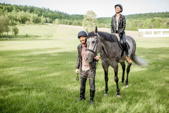 Man leading a horse with woman rider on the beautiful green meadow during the sunny weather