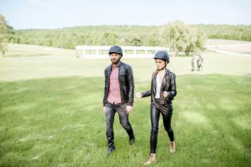 Young couple riders walking together after the horse ride outdoors on the green meadow