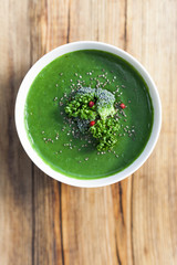Spinach green soup with broccoli in white bowl on wooden background top view.
