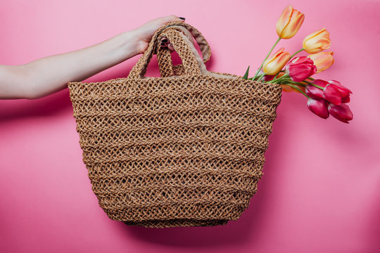 Studio shot of woman holding a straw bag with tulips on pink background. Spring sale in stores. Accessories - Powered by Adobe
