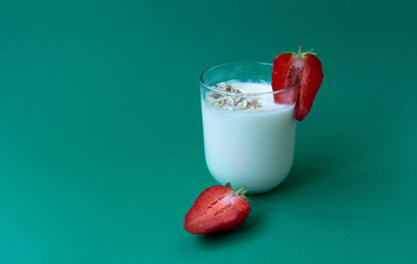 a glass of yoghurt with oatmeal flakes and strawberry slices on a green background. a glass of milk with strawberries.