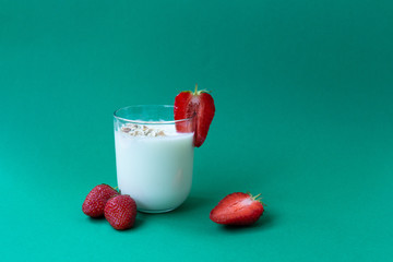 a glass of yoghurt with oatmeal flakes and strawberry slices on a green background. a glass of milk with strawberries.