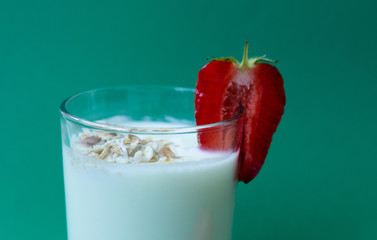 a glass of yoghurt with oatmeal flakes and strawberry slices on a green background. a glass of milk with strawberries.