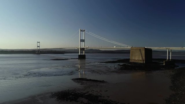 Drone rises slowly above river bed with the full width of Severn Bridge behind. Taken on a beautiful spring evening