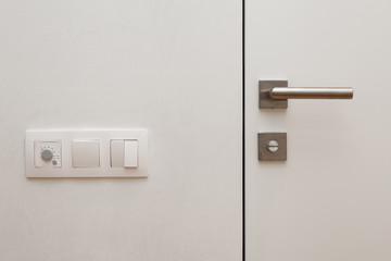 Obraz premium Light switch next to the white door with metallic handle