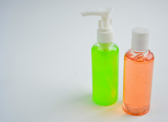 Two transparent plastic bottles with a green and pink liquid soap stand on a light background