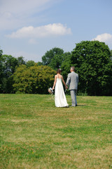 The bride and groom hold hands during the walking in the park. Wedding day in summer.