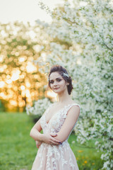 Fototapeta na wymiar Young beautiful brunette woman in blooming garden. Bride in wedding dress