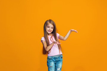 The happy teen girl presenting something, half length closeup portrait on orange background.