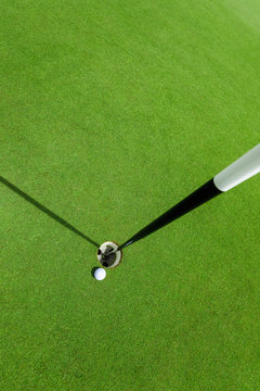 White golf ball near the hole on the green grass