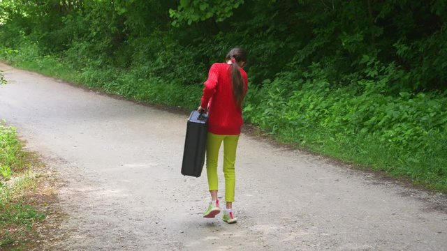 girl, walks through the woods with a heavy black suitcase. 4k, slow-motion shooting, steadicam shot.