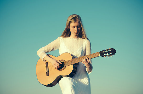 Fashion musician in white dress on sunny nature. Woman guitarist perform music concert. Albino girl hold acoustic guitar, string instrument. Sensual woman play guitar on blue sky
