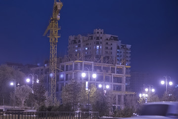 Fototapeta premium high buildings under construction with cranes at evening . Lightening multi-storey buildings under construction and cranes at night. building under construction against evening cloudy sky