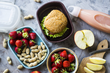 Cooking lunch for the child to school. On the gray kitchen table. Sandwich, strawberries and peanuts in lunchboxes. Top view.