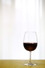 Single Red Wine in Bordeaux-shaped glass on Right Side of Copper Counter Top, with defocused Window and White Curtain, plain background, No decoration, Ambient Nature Day Lighting Studio image 1
