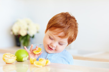 cute redhead toddler baby tasting orange slices and apples at the kitchen