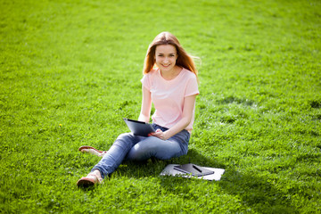 Girl with tablet sitting on the lawn and smiling