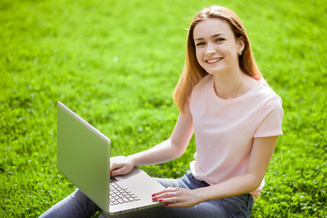 Girl with laptop sitting on the grass and smiling
