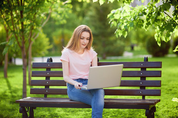 Obraz premium Girl with a laptop sitting on a bench in the Park