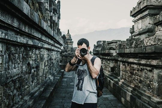 Handsome young tourist feeling the peace and taking some pictures of the great Borobudur temple, historical famous place in the java island Indonesia. Lifestyle and travel photography.