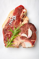 One raw piece of beef meat with bone. steak t bone with rosemary, salt, pepper on white background top view. The best piece of meat eight weeks maturation.