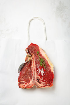 One Raw Piece Of Beef Meat With Bone. Steak T Bone With Rosemary, Salt, Pepper On White Background Top View. The Best Piece Of Meat Eight Weeks Maturation.