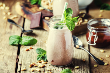 Chocolate milkshake or cocktail with nuts and mint leaves, old wooden background, selective focus
