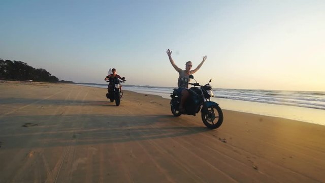 Two crazy tourists riding on a motorbike without hands.