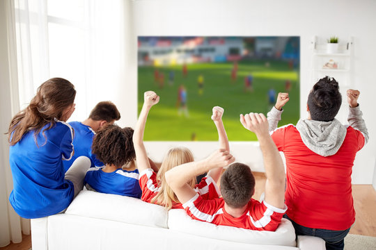 sport, leisure and entertainment concept - friends or football fans watching soccer on projector screen at home, one team wins another loses