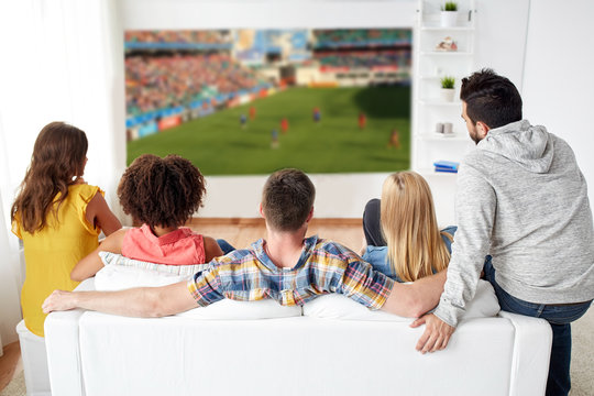 sport, leisure and entertainment concept - friends or football fans watching soccer game on projector screen at home