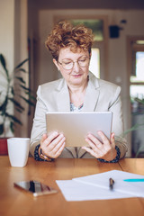 portrait of an attractive middle aged woman holding a tablet. fashionable mature lady using a tablet in her home office, working from home as a creative. businesswoman reading email at home.