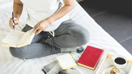 Fototapeta premium Young woman sitting working and writing in the notebook on bed leisure concept taking notes, Comfortable female workplace. Memories, planning , education.