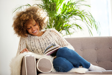 attractive african american woman sitting on sofa reading book