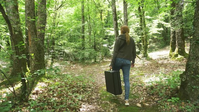 girl, walks through the woods with a heavy black suitcase. 4k, slow-motion shooting, steadicam shot.
