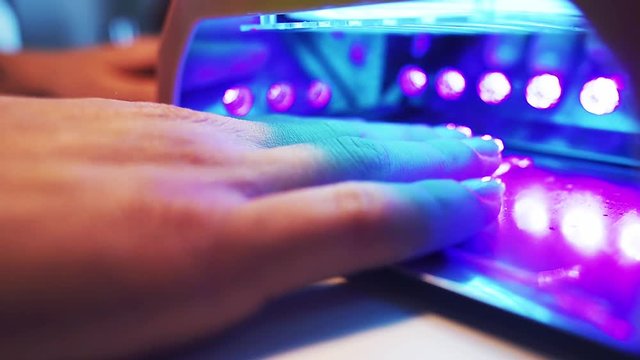 Close-up of woman holding her hand in led lamp to dry the gel nail polish. Hand in drying tool. Slow motion.