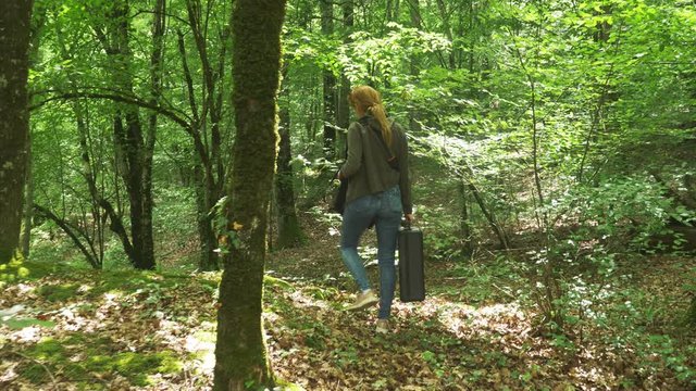 girl, walks through the woods with a heavy black suitcase. 4k, slow-motion shooting, steadicam shot.