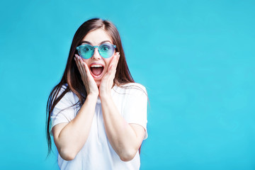 Pretty caucasian brunette girl wears sunglasses have happy surprised face expression on blue background
