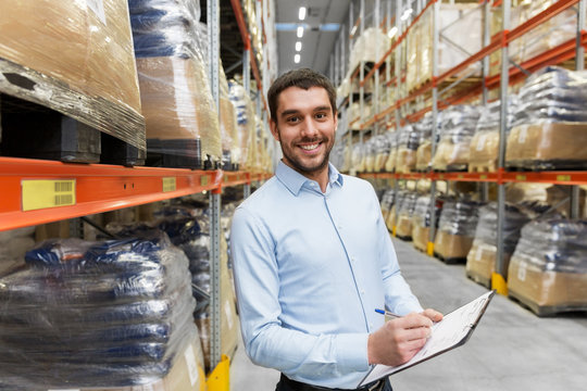 logistic business, shipment and people concept - happy businessman with clipboard at warehouse