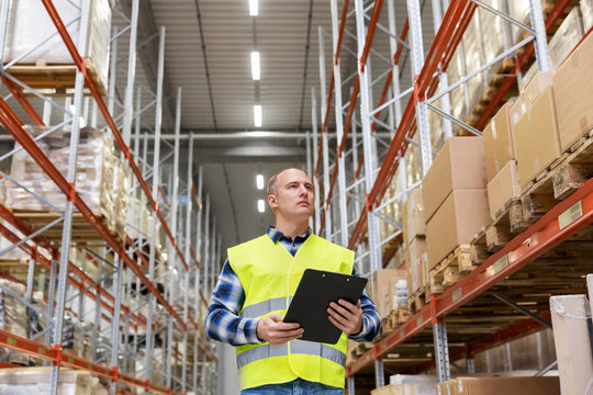 logistic business, shipment and people concept - male worker or supervisor with clipboard in reflective safety vest at warehouse