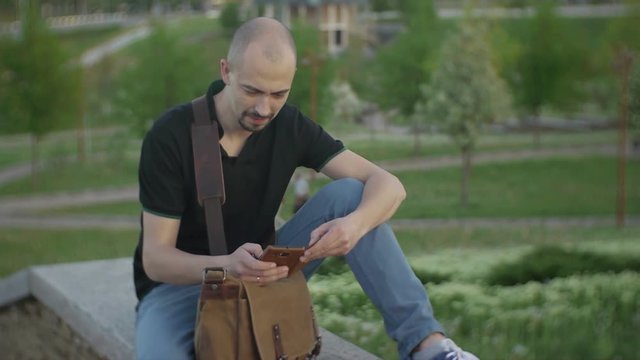 Attractive male sidia in a city park on a summer day uses the Internet with a smartphone