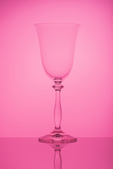 Glasses on a high leg, on the mirror surface of the table, on a pink background. Graphic composition, rhythm.