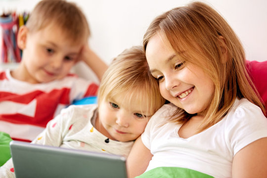 childhood, technology and family concept - happy little kids with tablet pc computer in bed at home