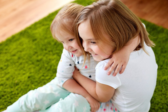 childhood, family, expressions and people concept - happy little girls or sisters hugging at home
