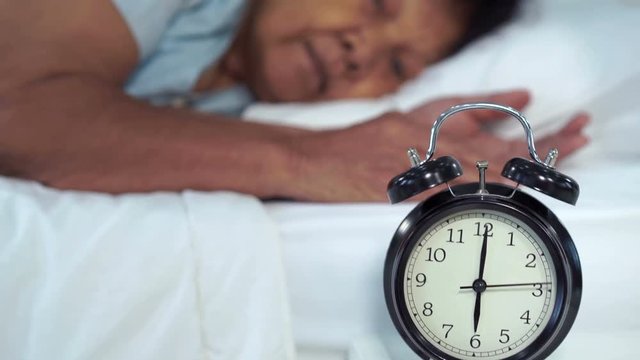 senior woman in bed pressing snooze button on early morning alarm clock