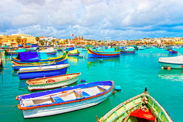 Fototapeta na wymiar Luzzu boats in Marsaxlokk Port embankment at bay Mediterranean sea