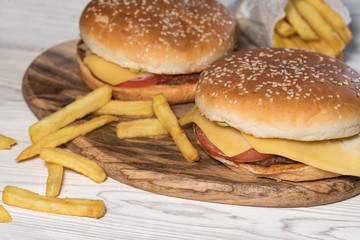 Two cheeseburgers on sesame buns with juicy beef patties and fresh salad ingredients served with French fries on a rustic wooden table