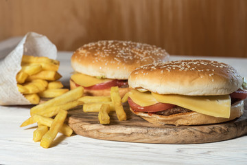 Two cheeseburgers on sesame buns with juicy beef patties and fresh salad ingredients served with French fries on a rustic wooden table