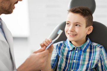 medicine, dentistry and healthcare concept - male dentist giving toothbrush to kid patient at dental clinic